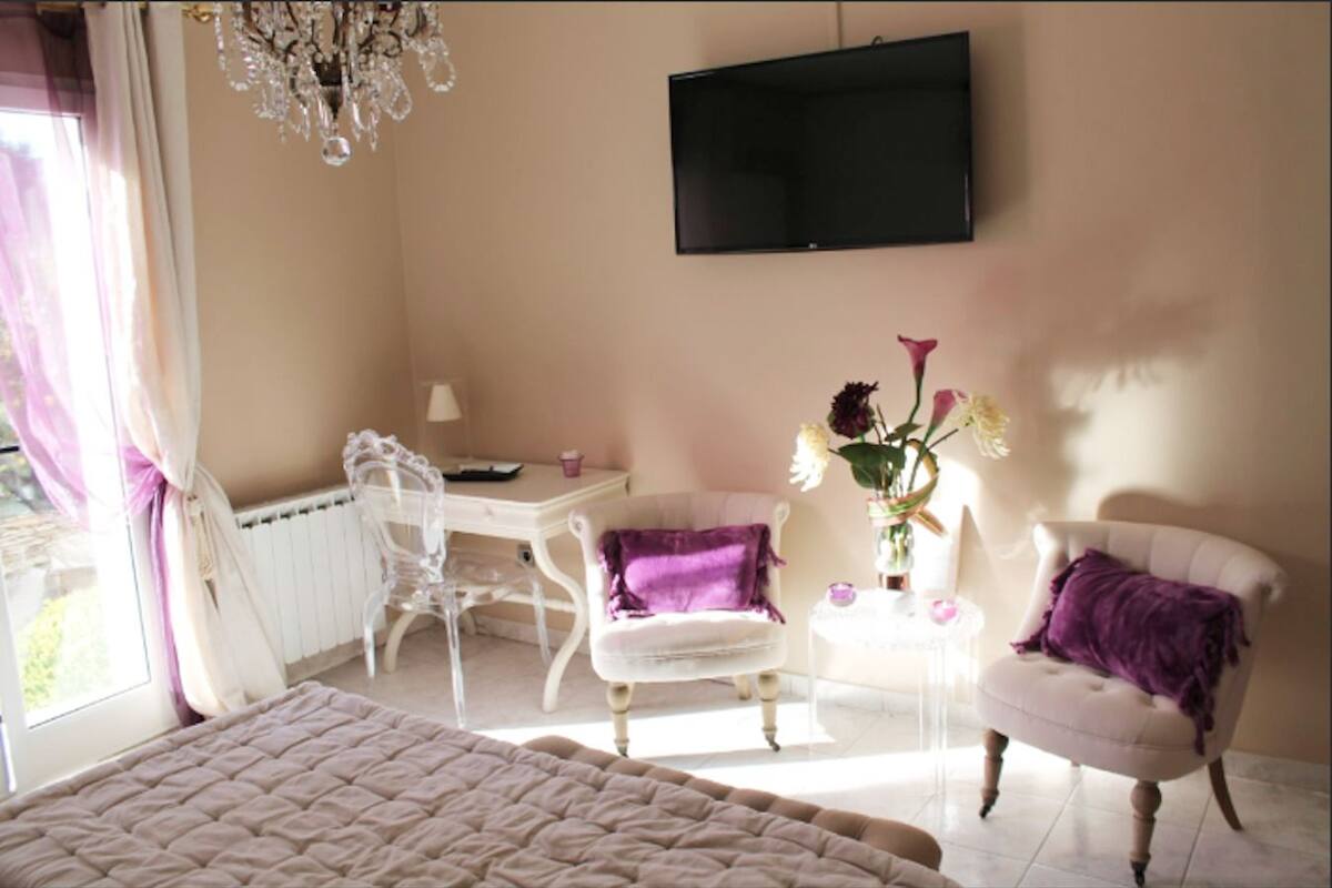 Ein Schlafzimmer mit Bett, Schreibtisch, Stuhl, Fernseher und einem Fenster mit Vorhängen.