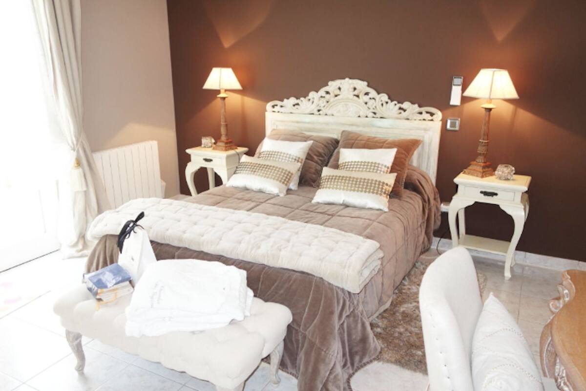 Ein Schlafzimmer mit einem großen Bett, zwei Nachttischen inklusive Lampen, einer Bank und einem Stuhl.