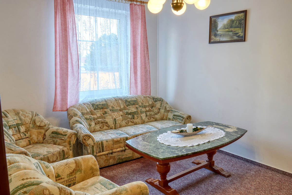 Una habitación con un sofá estampado, una mesa redonda con un mantel de encaje y un cuadro en la pared.