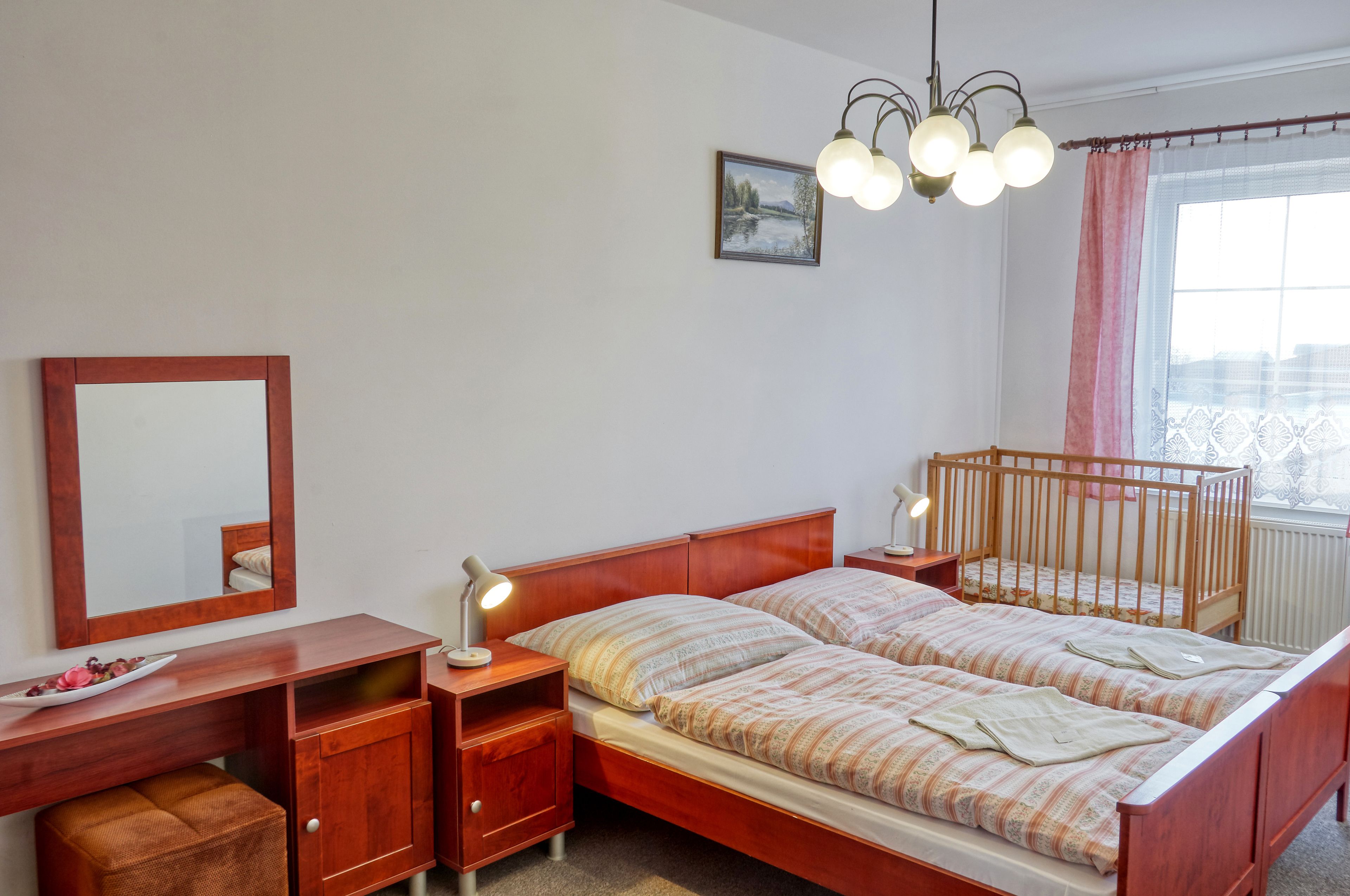 Een slaapkamer met een houten bed, nachtkastjes, een bureau, een spiegel en een raam met gordijnen.
