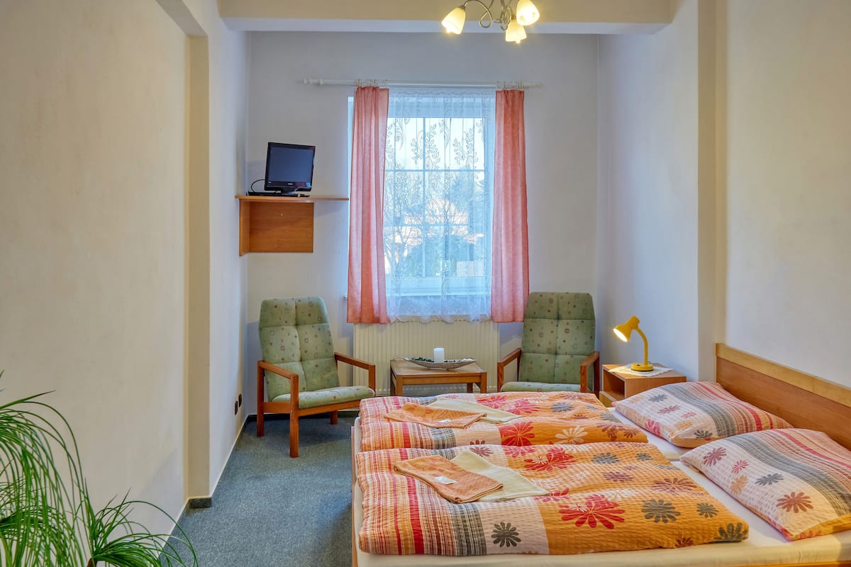 Una habitación pequeña y acogedora con una cama, dos sillas, un escritorio y un televisor.
