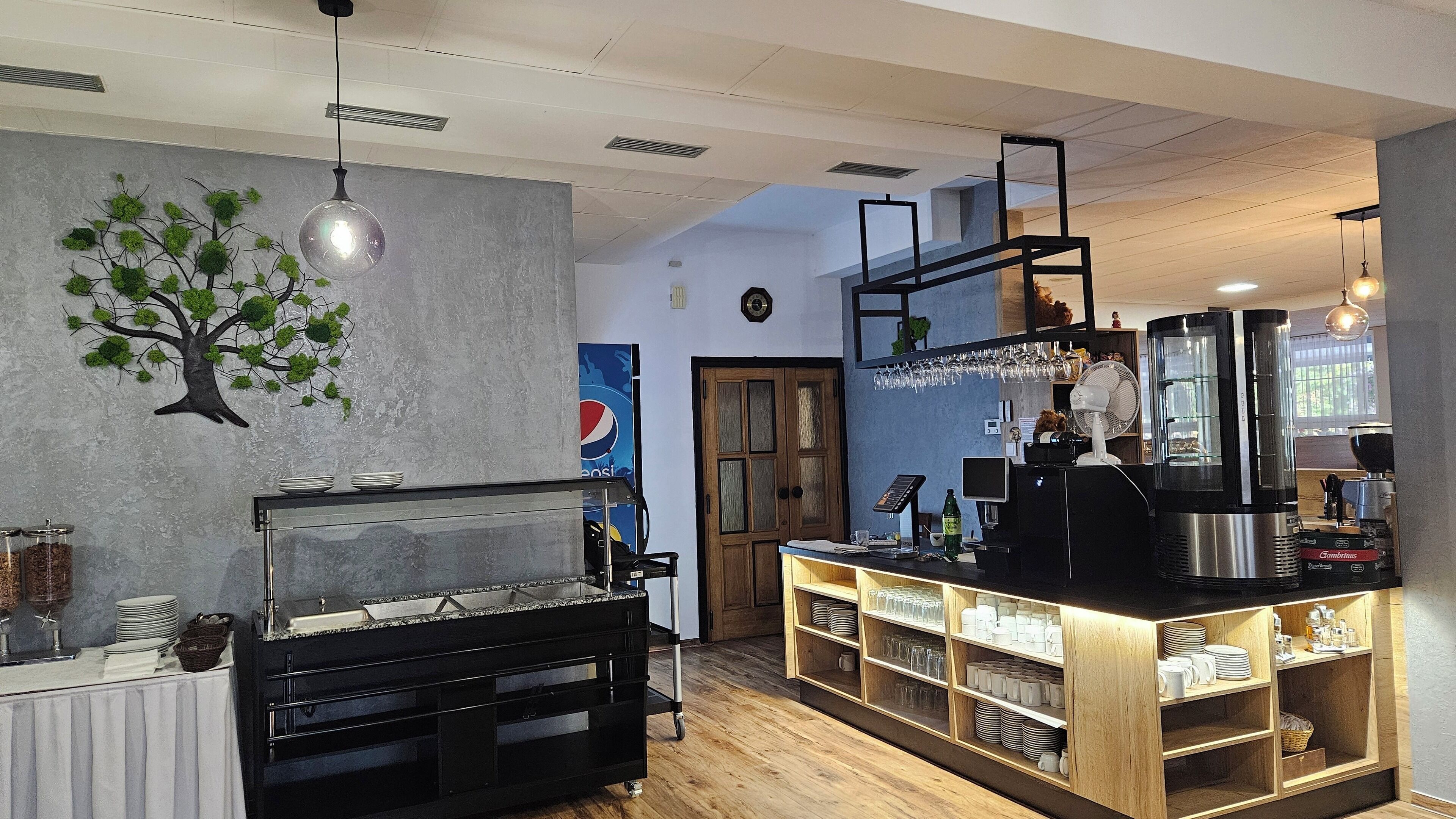 L’intérieur d’un restaurant avec un comptoir en bois, une décoration murale représentant un arbre et un ventilateur de plafond.