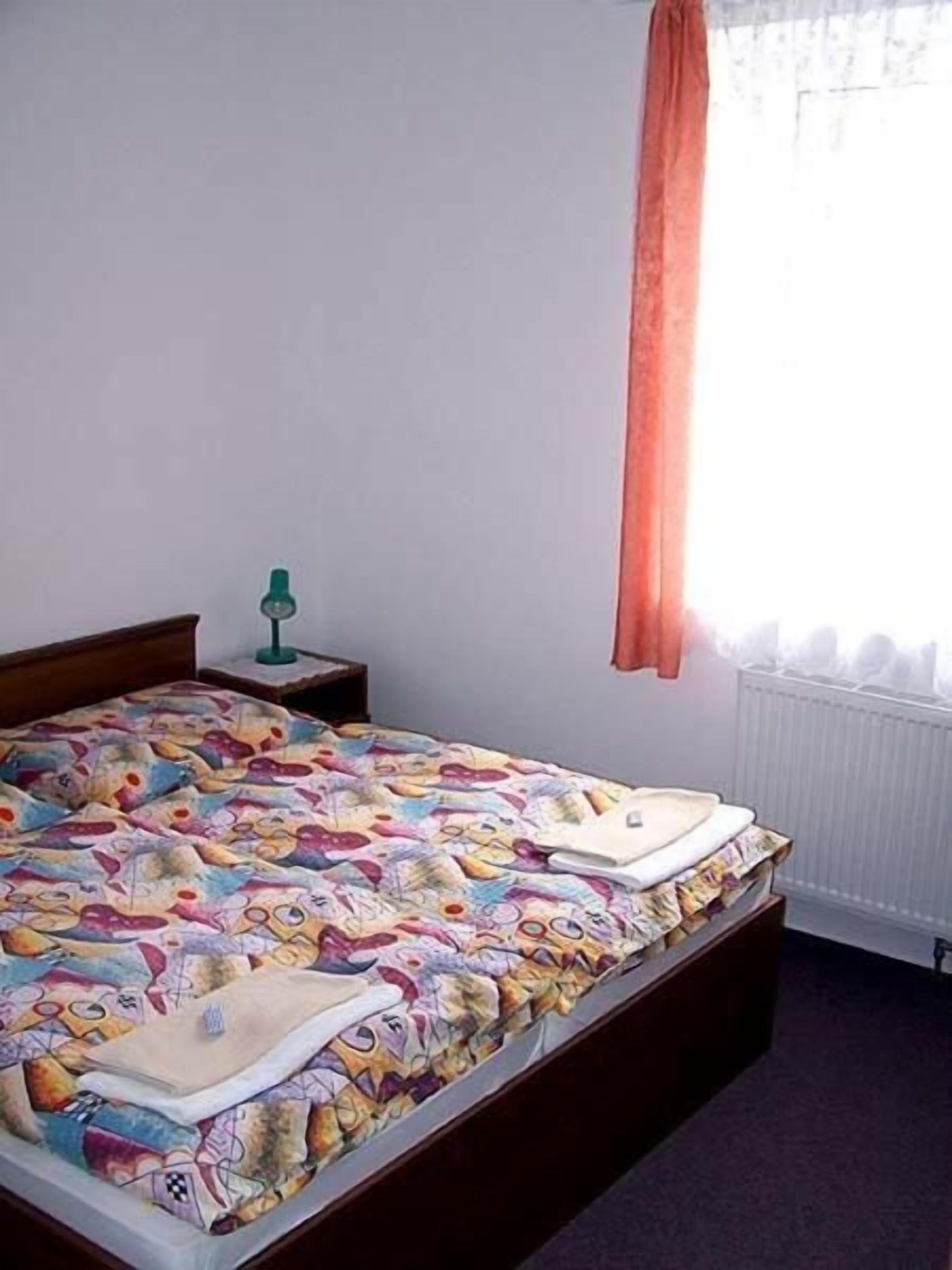 A bedroom with a bed, a nightstand, a lamp, and a window with curtains.
