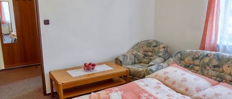 A bedroom with a bed, a wooden nightstand, a chair, and a small table with a bowl of fruit.
