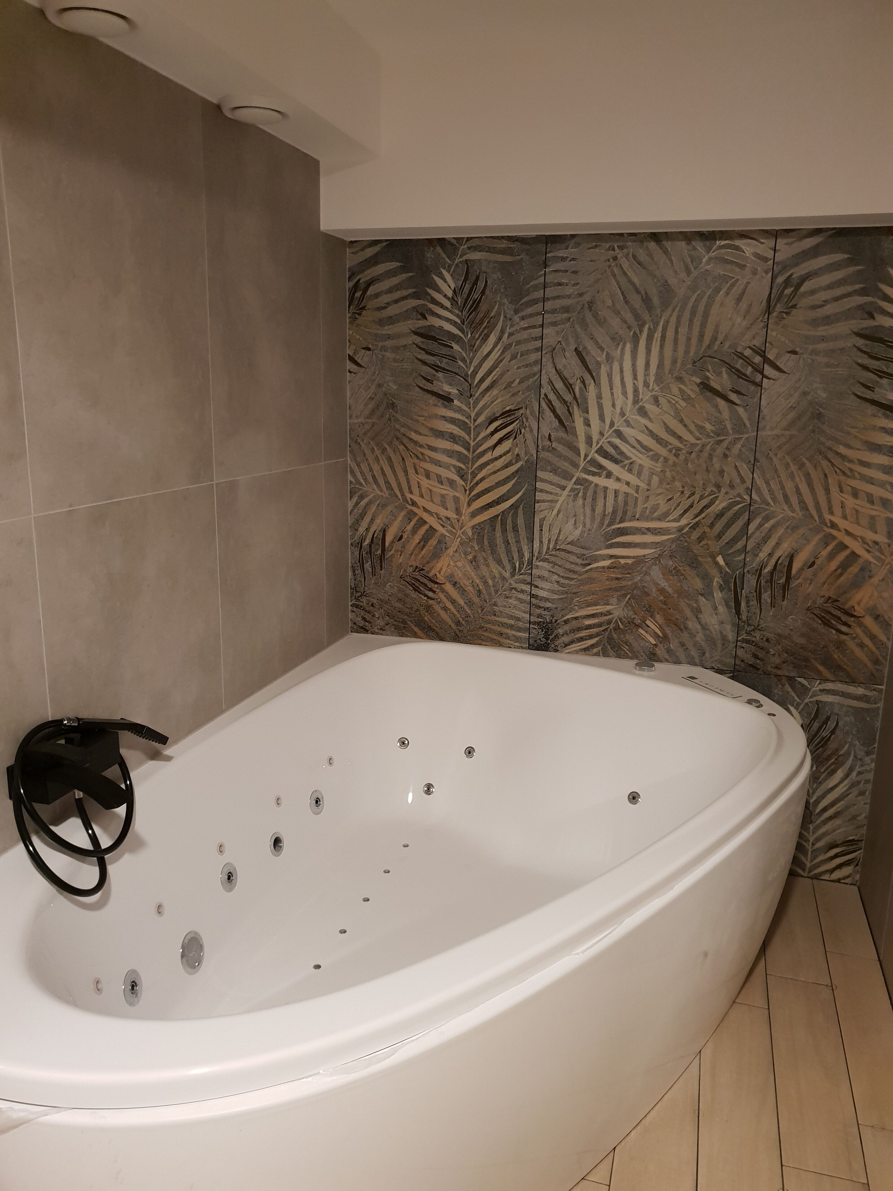 Un baño moderno con una bañera independiente, paredes cubiertas de azulejos y una pared decorativa con diseño de hojas.