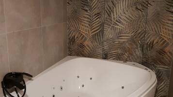 Un baño moderno con una bañera independiente, paredes cubiertas de azulejos y una pared decorativa con diseño de hojas.