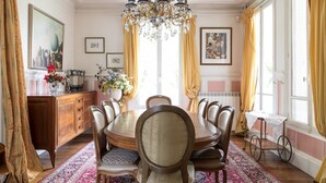 A dining room with a large wooden table, six chairs, a chandelier, and a patterned rug. - Le Colombier (Neuilly-Plaisance)