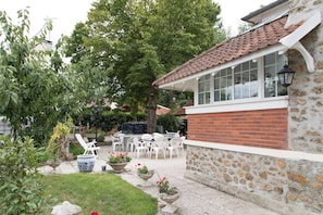 A stone building with a tiled roof, a patio with white chairs and tables, and potted plants. - Le Colombier (Neuilly-Plaisance)