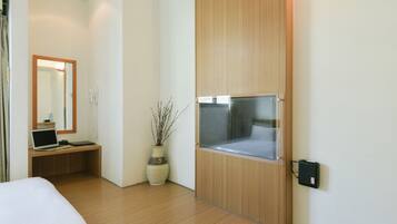 Habitación de hotel con cama, escritorio con computadora portátil, un jarrón con ramas, armario de madera y un dispositivo montado en la pared.