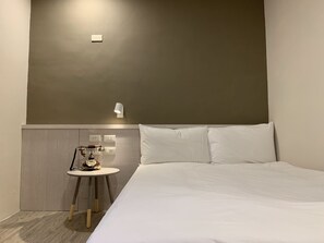 A hotel room with a bed, a small table with a clock, and a wall-mounted light fixture. - Raise Hotel Taichung (Taichung)