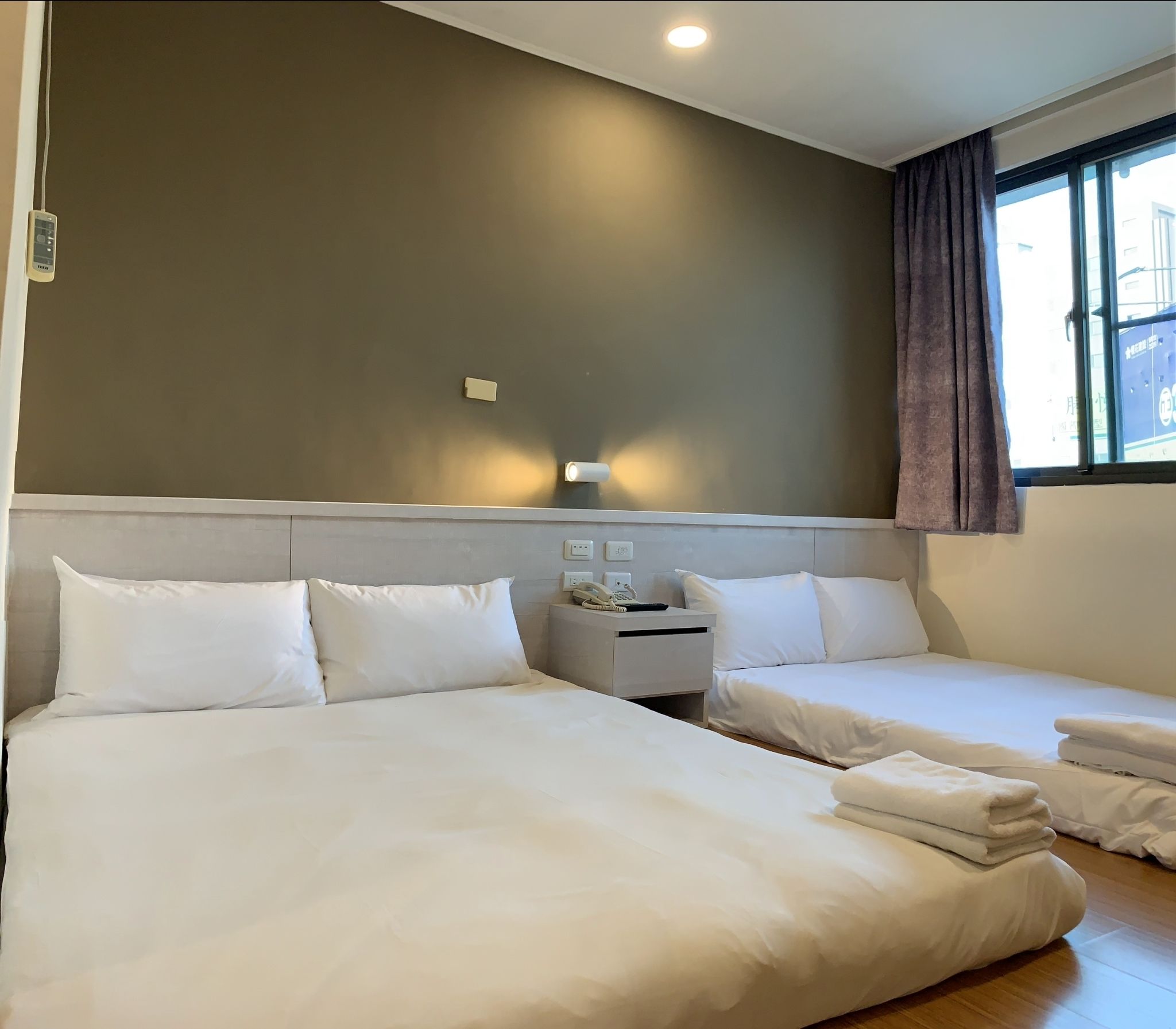 Una habitación de hotel con dos camas, una mesita de noche con teléfono y una ventana con cortinas.