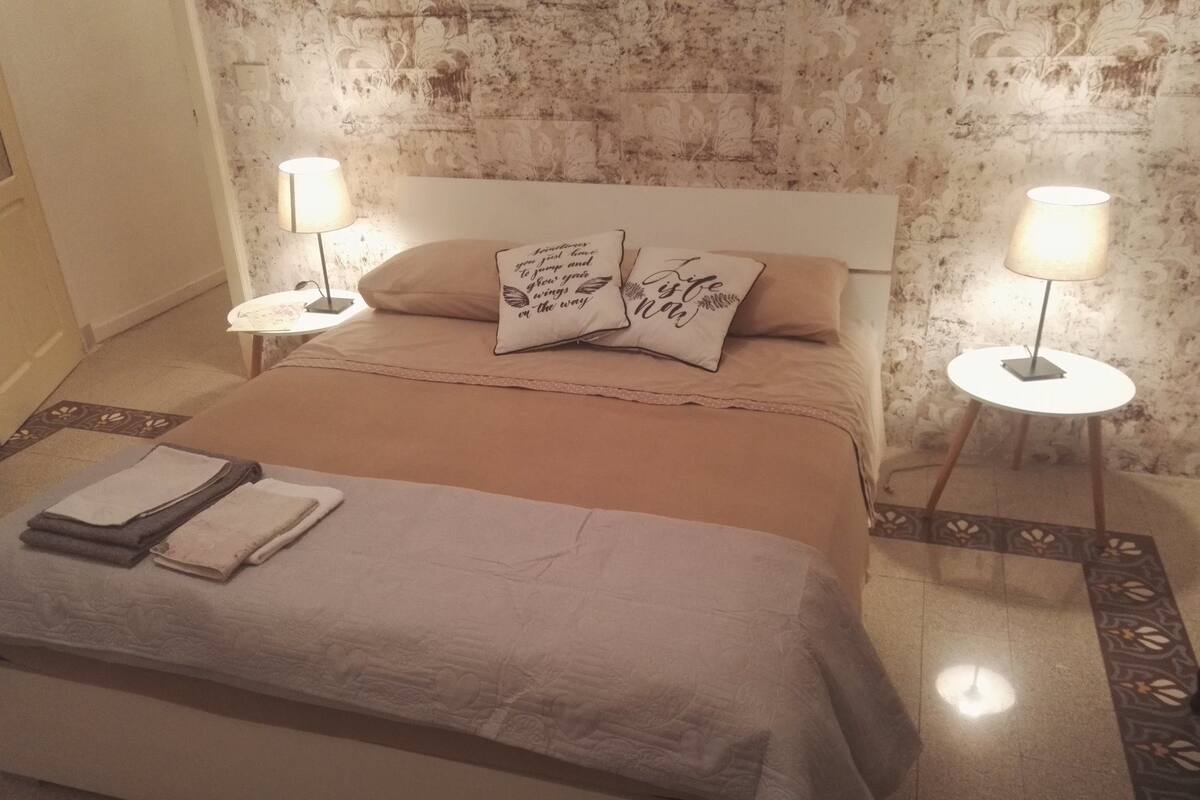 A neatly made bed with pillows, two bedside tables with lamps, and a patterned rug.