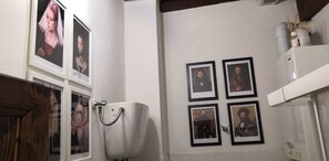 A bathroom with a toilet, a sink, and framed pictures on the wall. - Camere Mazzini 49 (Sansepolcro)
