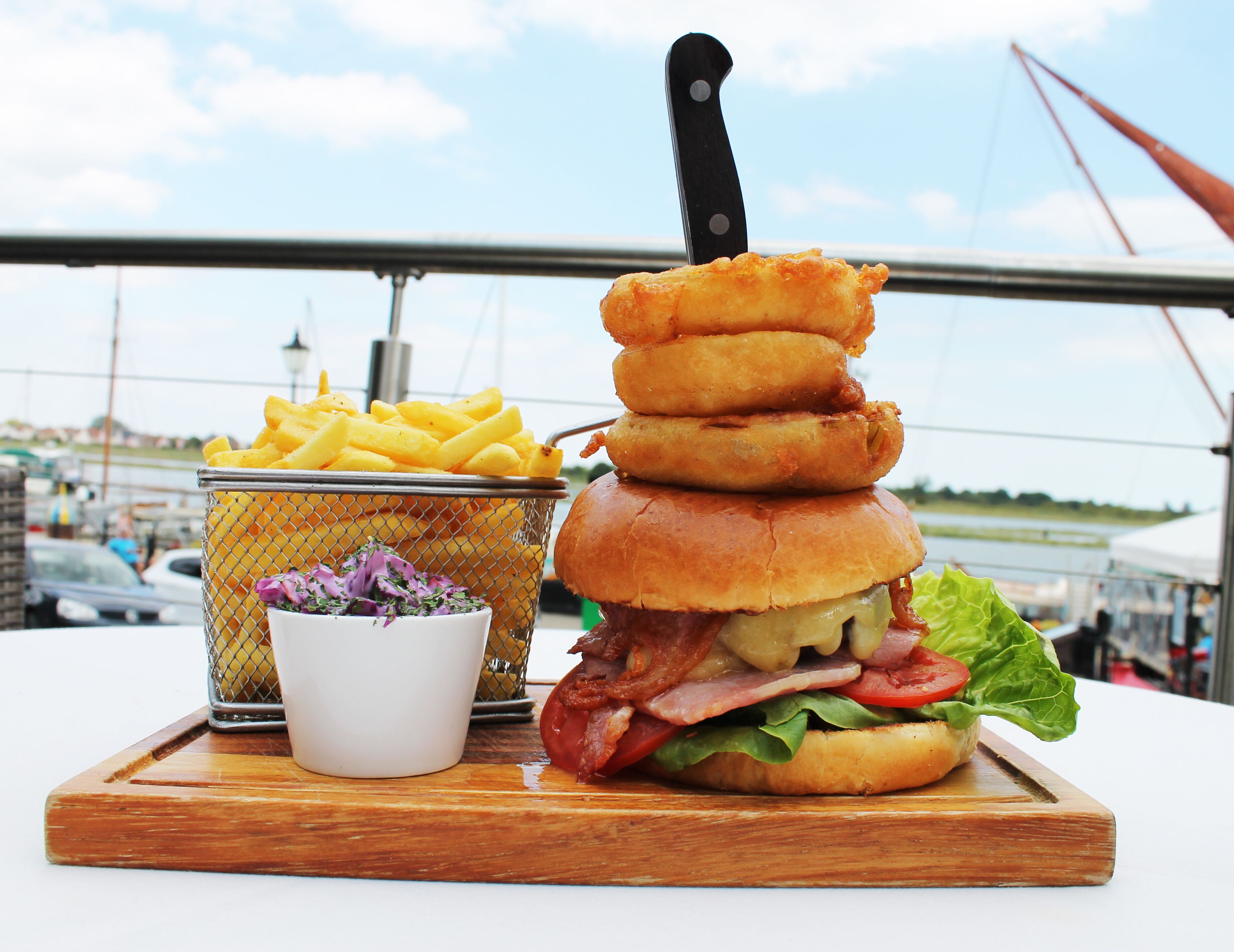 A meal consisting of a burger, French fries, and a small bowl of salad on a wooden board.