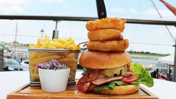 A meal consisting of a burger, French fries, and a small bowl of salad on a wooden board.