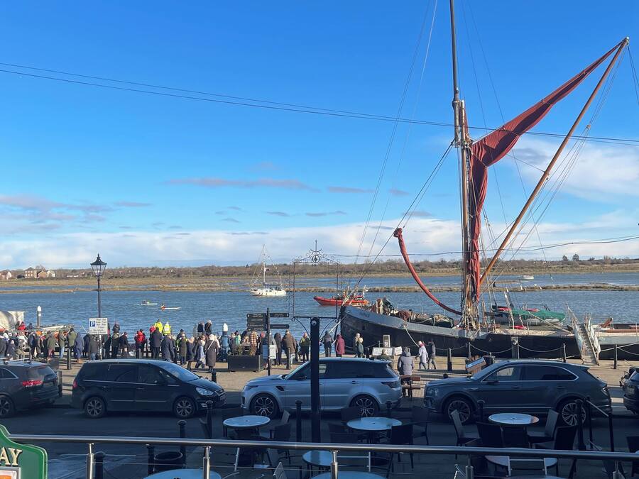 A waterfront café with outdoor seating, a view of the sea, and boats in the background.