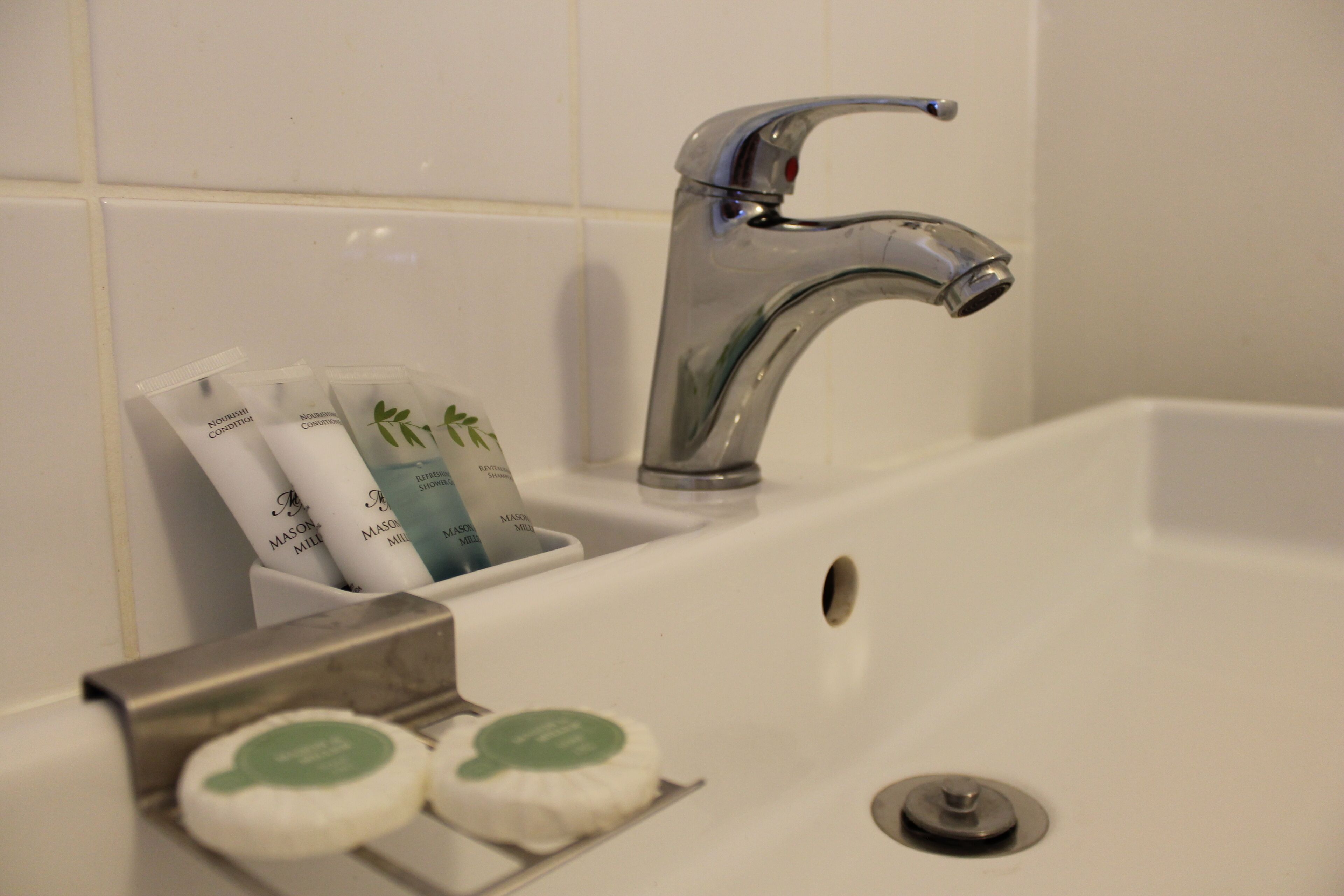 Un lavamanos de baño con un grifo moderno, un jabonera y un recipiente con artículos de aseo.