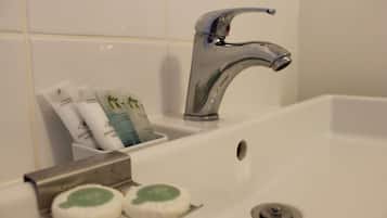 Un lavamanos de baño con un grifo moderno, un jabonera y un recipiente con artículos de aseo.