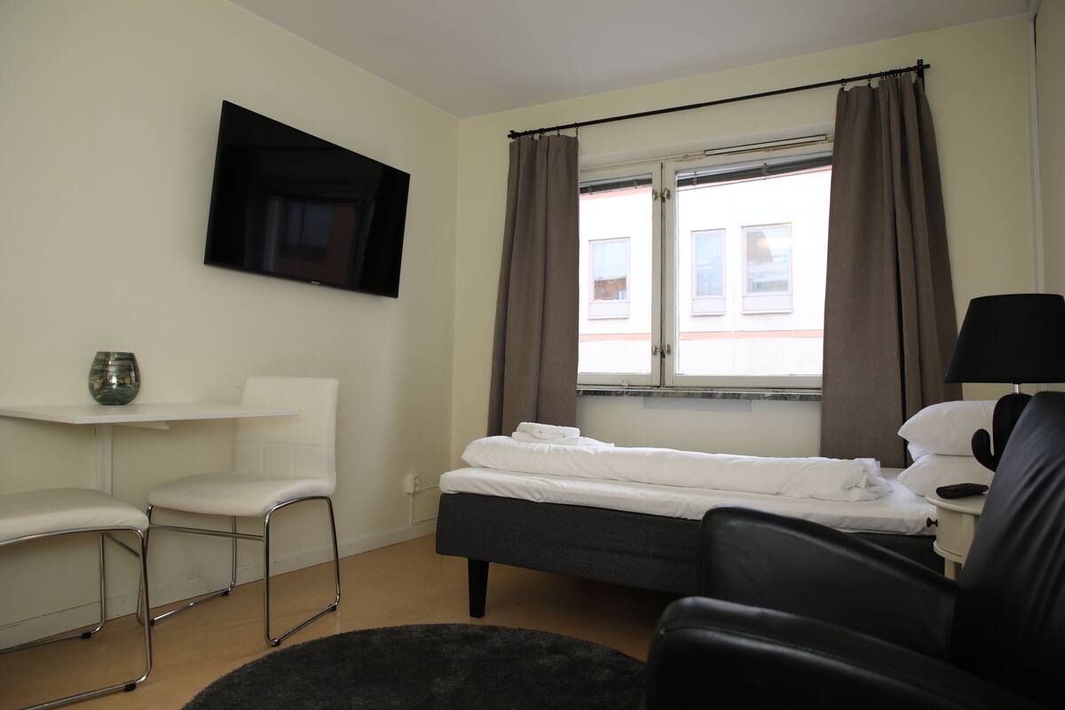 A hotel room with a bed, a desk, a chair, a TV, and a window with curtains.