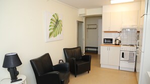 A compact living space with a kitchenette, two black leather chairs, a small white side table with a lamp, and a large leaf artwork on the wall. - Fastliving Apartment Hotel (Vasteras)