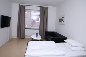 A hotel room with a bed, a black sofa, a small table with a remote control, and a window with curtains. - Fastliving Apartment Hotel (Vasteras)