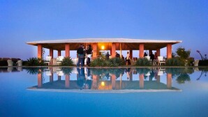 Un espacio al aire libre techado con piscina, mobiliario y una estructura con columnas.