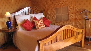 Una cama de madera con cabecera, una mesita de noche con lámpara y una alfombra estampada.