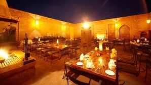 Un área de comedor al aire libre con varias mesas y sillas, iluminada con una cálida luz.