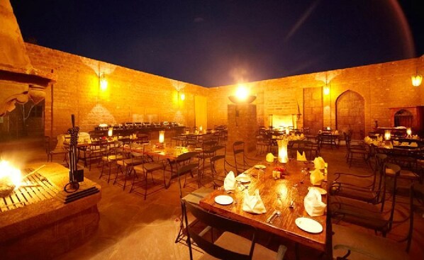 An outdoor dining area with multiple tables and chairs, illuminated by warm lighting.