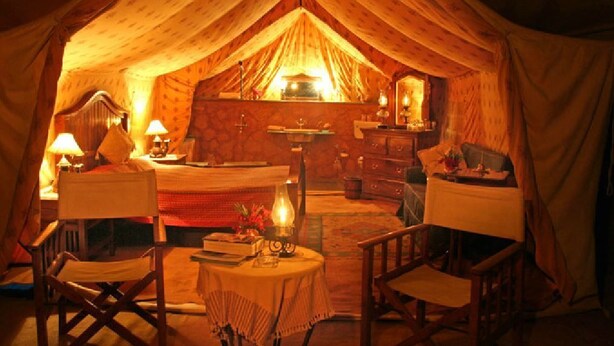 Una habitación tipo tienda de campaña, acogedora, con una cama, dos sillones, una mesita y un espejo.