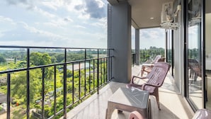 A balcony with a view of greenery and a distant landscape. There are two chairs and a table.