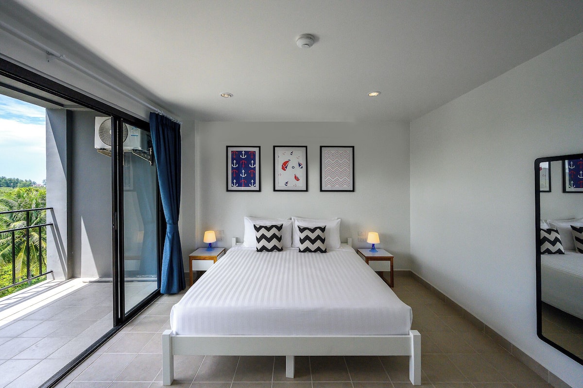 Une chambre d’hôtel moderne avec un grand lit, un balcon offrant une belle vue et des œuvres d’art accrochées aux murs.
