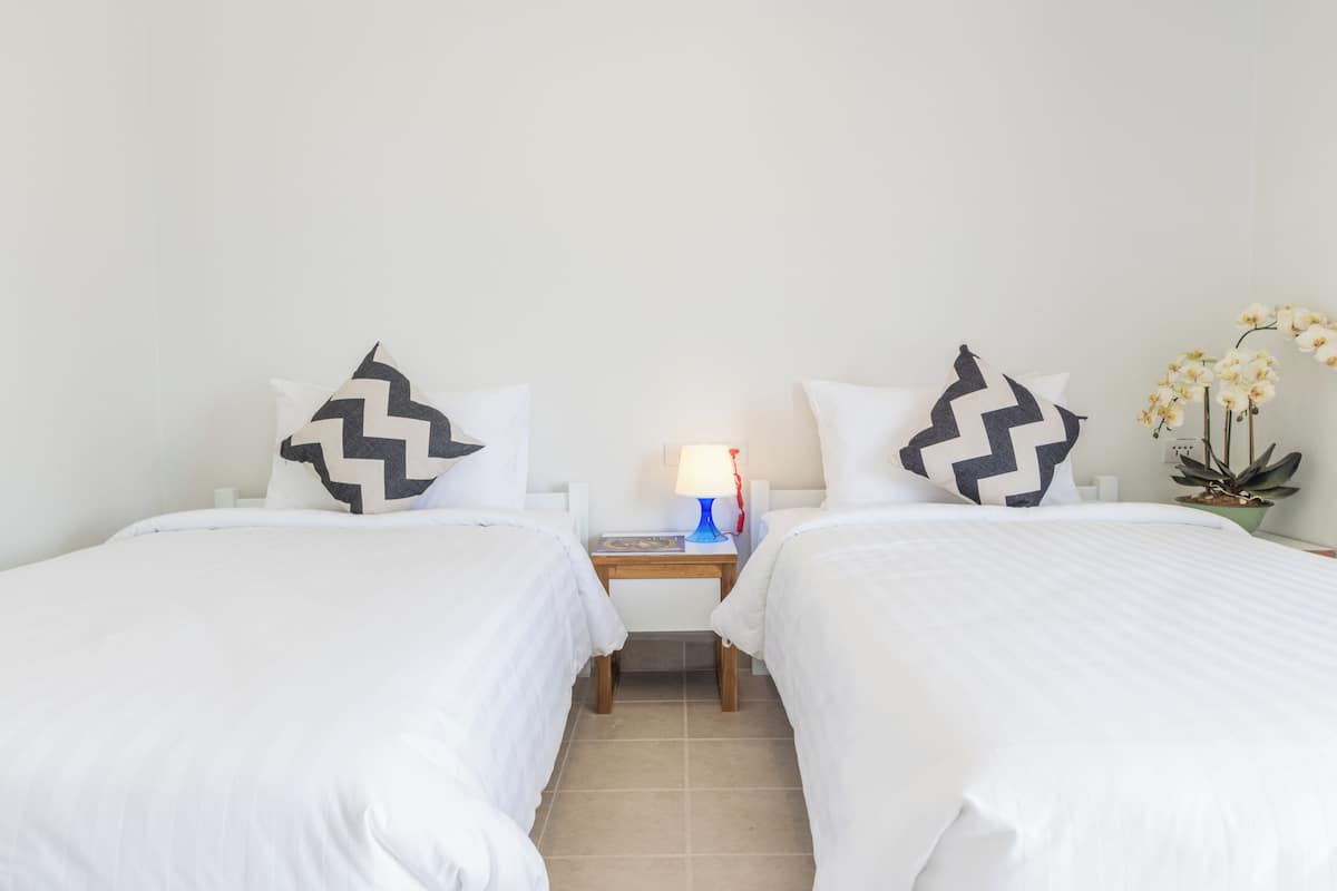 Une chambre d’hôtel avec deux lits simples, une table de chevet avec une lampe et une petite table.