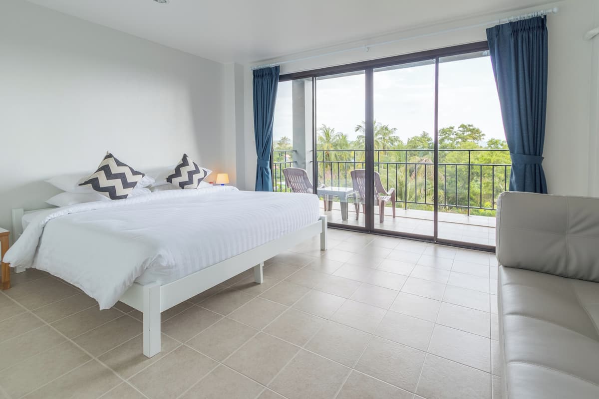 Une chambre avec un grand lit, un balcon avec des chaises et une vue sur la verdure.