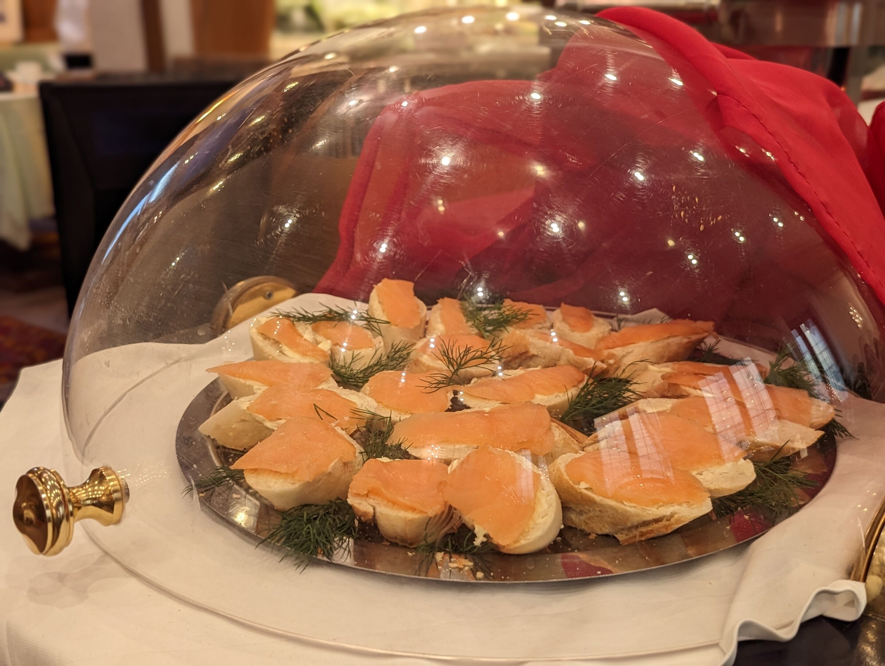 A glass dome-covered food display with salmon and bread garnished with dill.