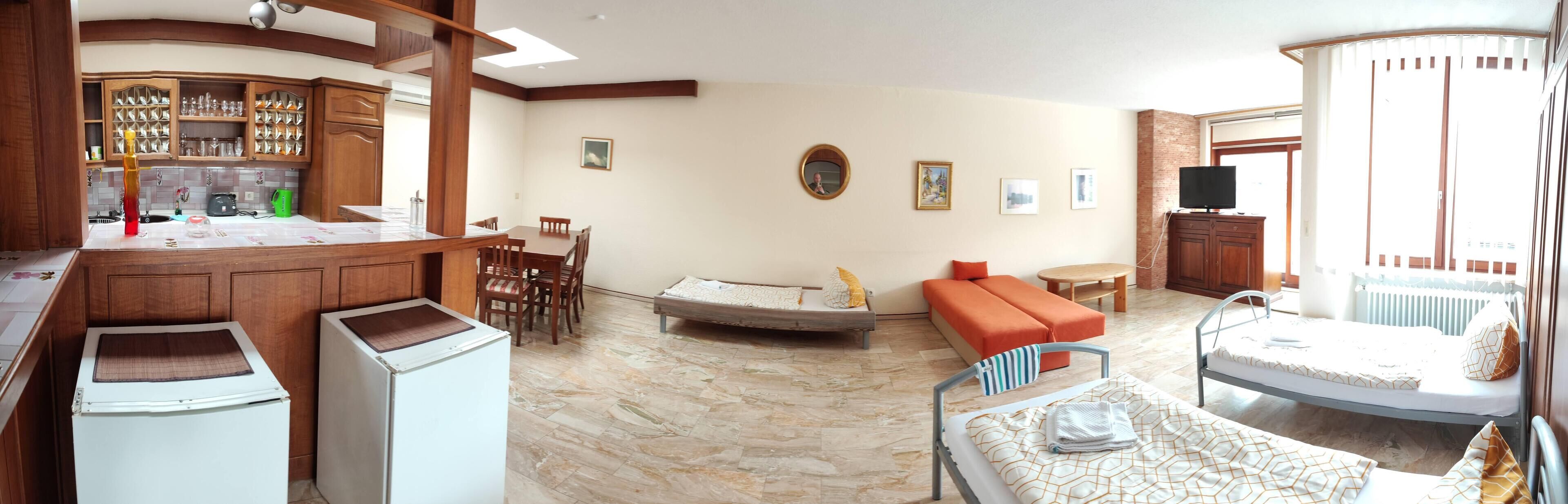 Uma sala ampla com cozinha, mesa de jantar, sofá e uma cama.