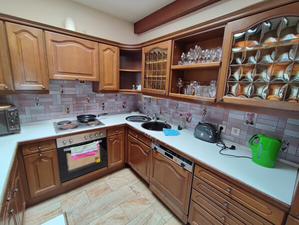 A kitchen with wooden cabinets, a sink, a stove, and a dishwasher. - Hotel Schiff (Rastatt)