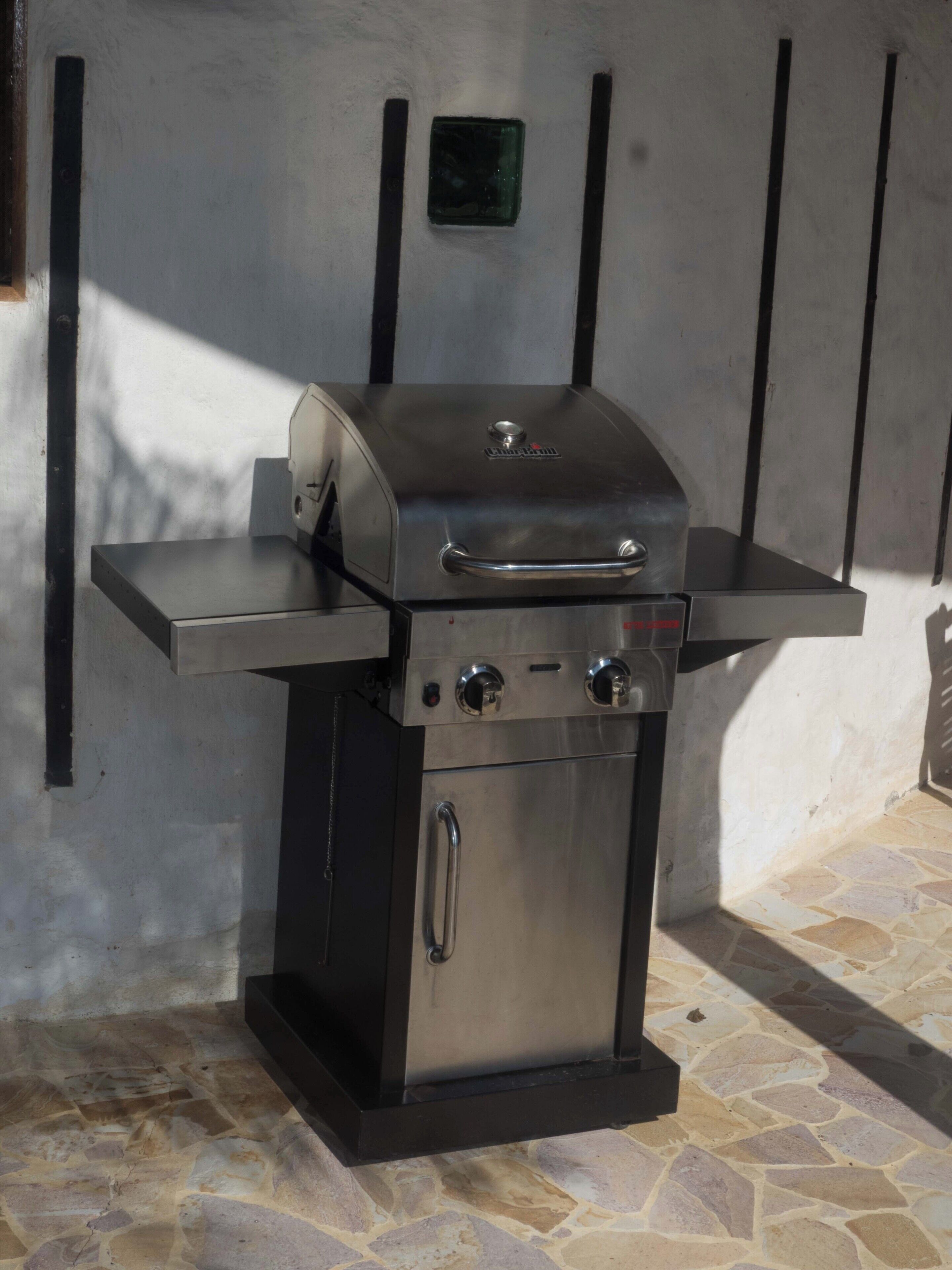 A stainless steel barbecue grill with a side table, a control panel, and a vent hood.