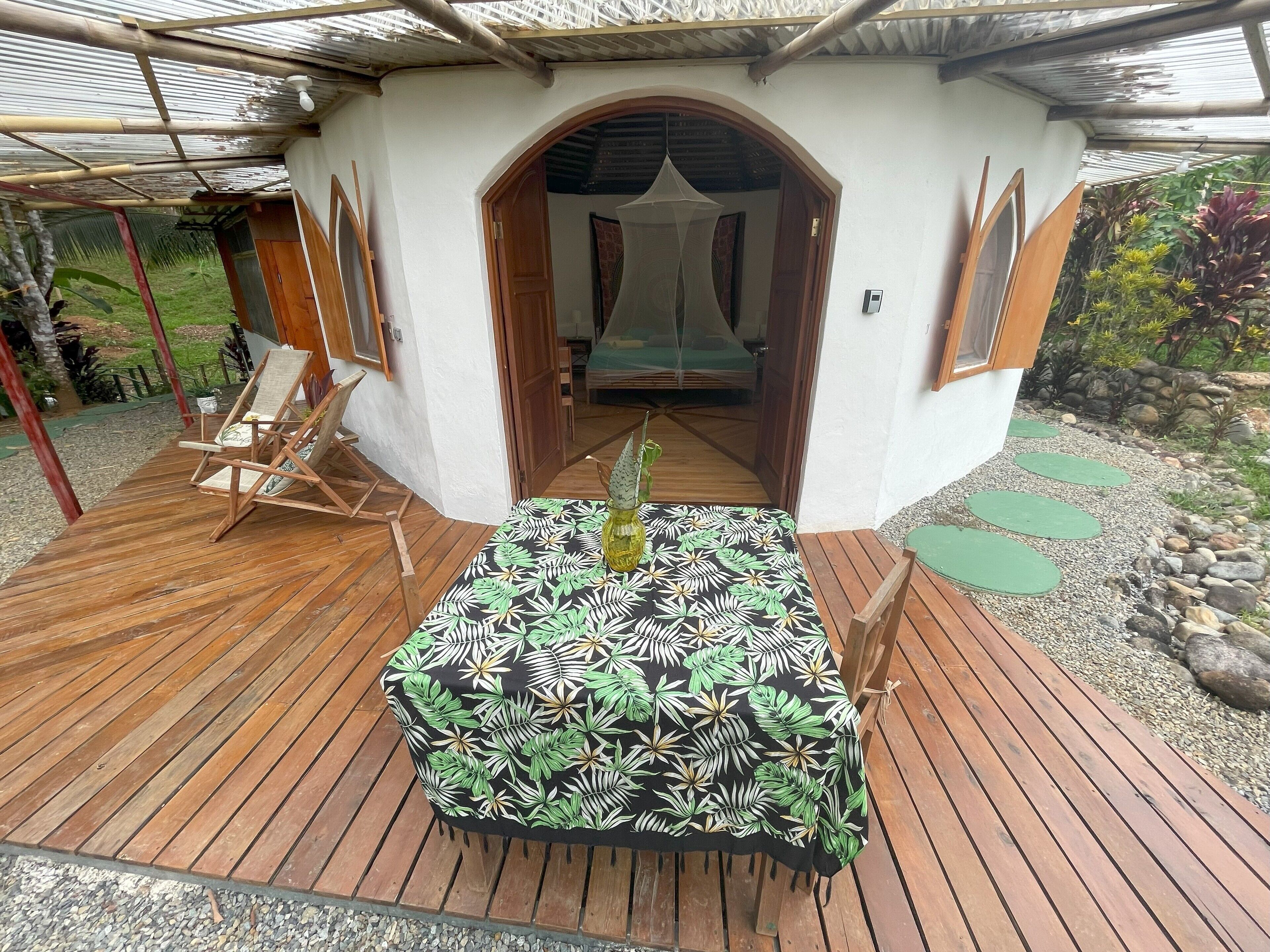 A wooden deck with a table and chairs, an arched doorway, and a garden area with plants and a stone path.