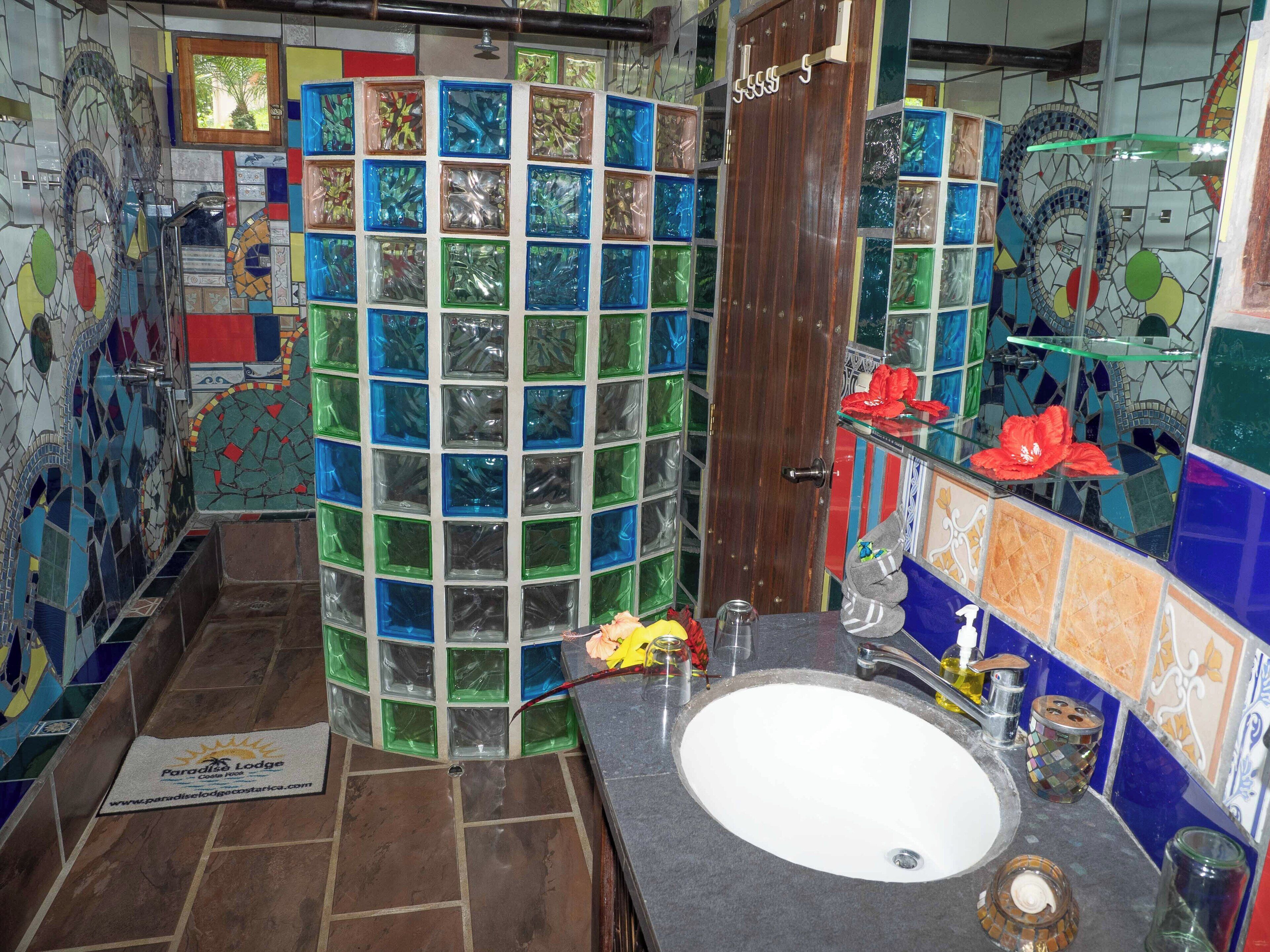 A bathroom with a mosaic tile wall, a wooden door, a sink, and a glass shower enclosure.