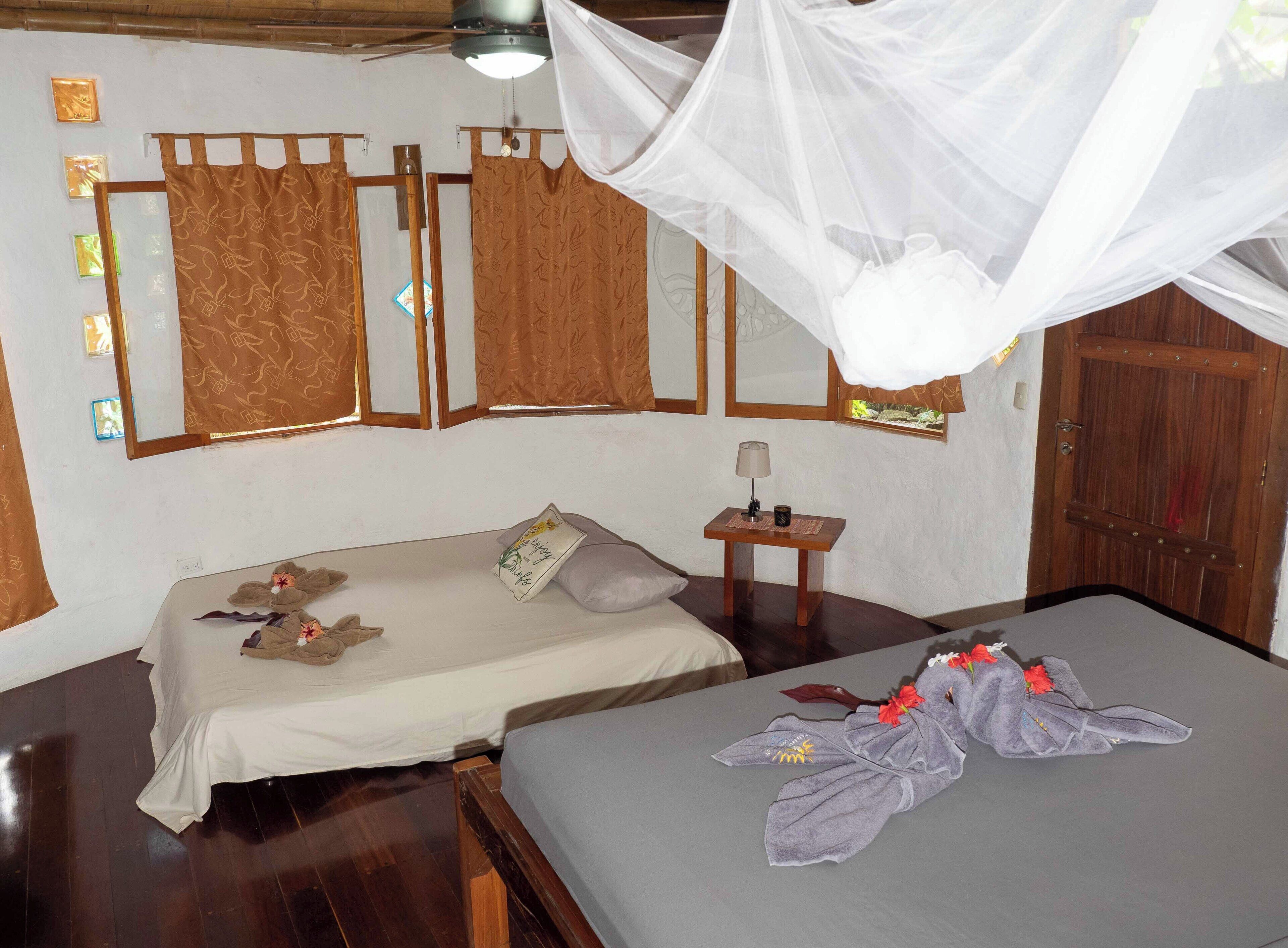 Quarto com duas camas, uma mesinha com abajur e uma porta de madeira.