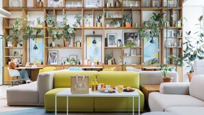 En moderne stue med sofa, sofabord og reoler fyldt med planter og bøger.