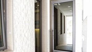 A hallway with a white textured wall, a glass door, and a tiled floor. - Boutique Hotel Arka (Budva)