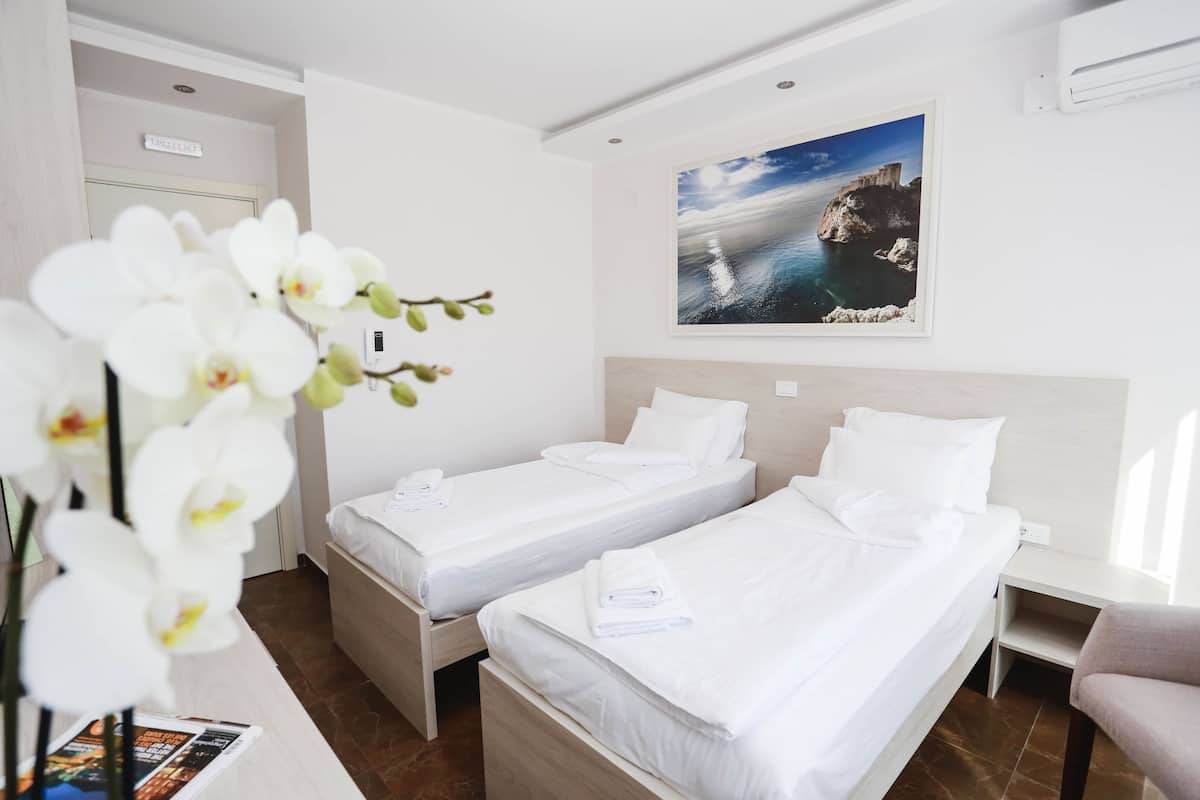 Ein Hotelzimmer mit zwei Betten, einem Holzkopfstück, einem gerahmten Foto von der Küste und einer Vase mit weißen Orchideen.