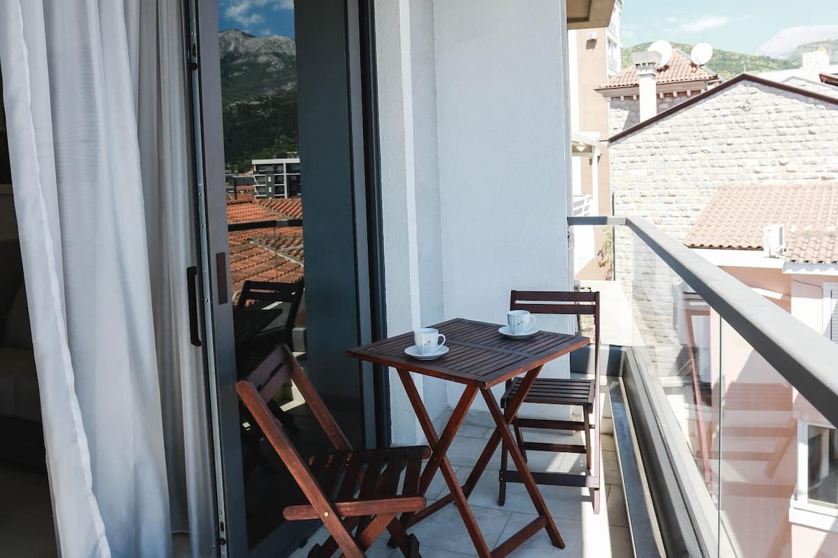 Ein Balkon mit Tisch und Stühlen, eine Schiebetür und Blick auf Gebäude und Berge.