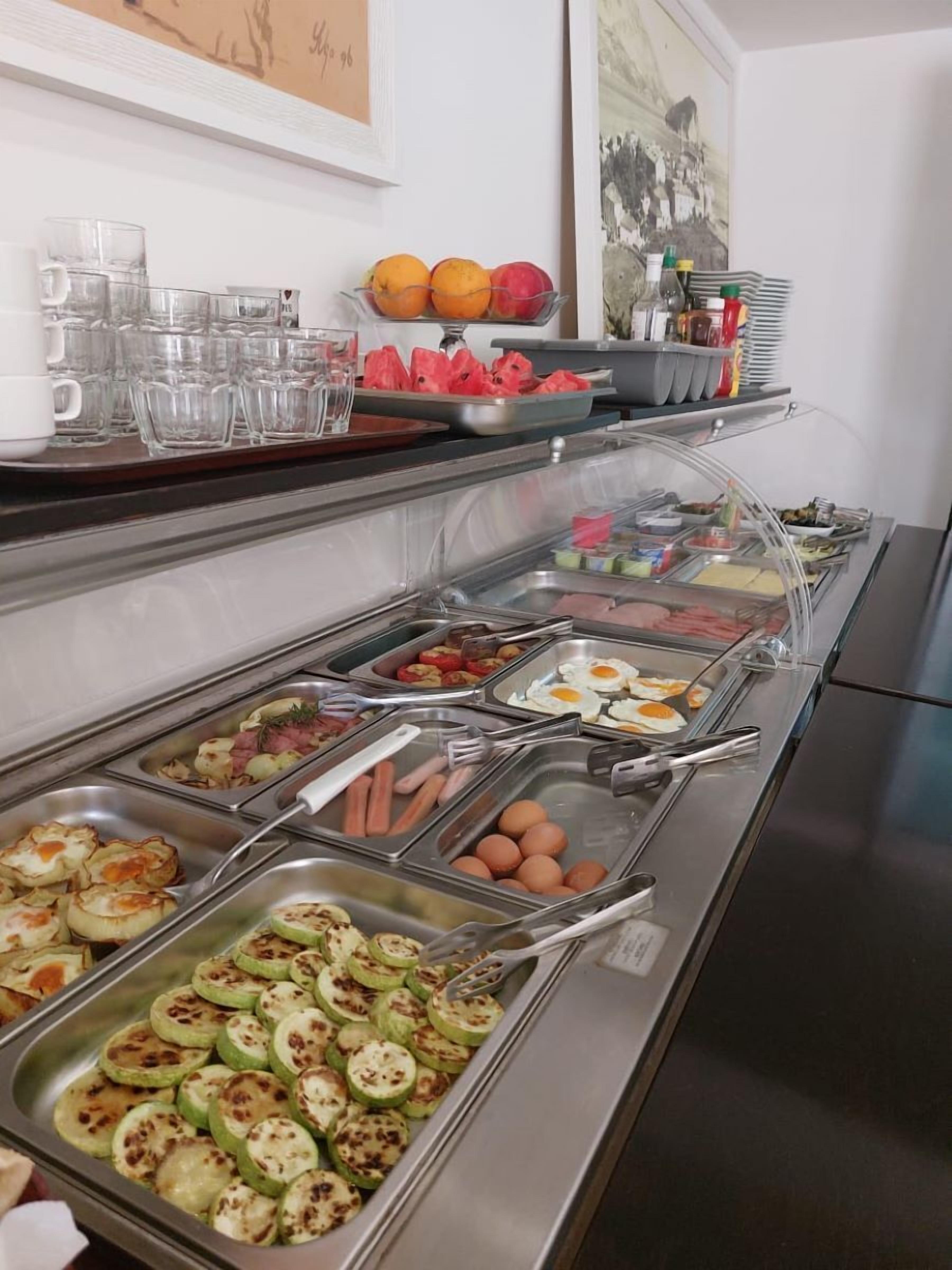 A buffet with various food options including eggs, sausages, and sliced vegetables.