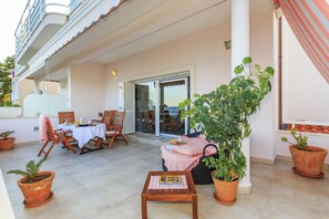 A covered outdoor patio with a table and chairs, potted plants, and a sliding glass door leading to an interior space. - Villa Lola (Okrug)