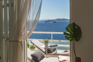 Un balcón con vista al mar, un barco a lo lejos y una planta en maceta.