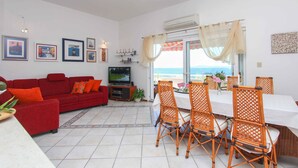 A living room with a red sofa, a dining table with wicker chairs, a TV, and artwork on the walls. - Villa Lola (Okrug)