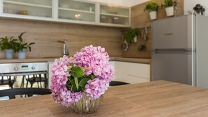 A modern kitchen with wooden cabinets, a stainless steel refrigerator, and a vase of pink flowers on the table. - Villa Lola (Okrug)